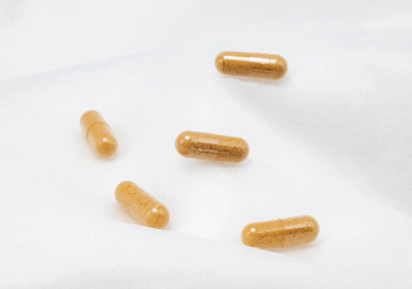 Capsule di integratore color ambra su una superficie bianca.